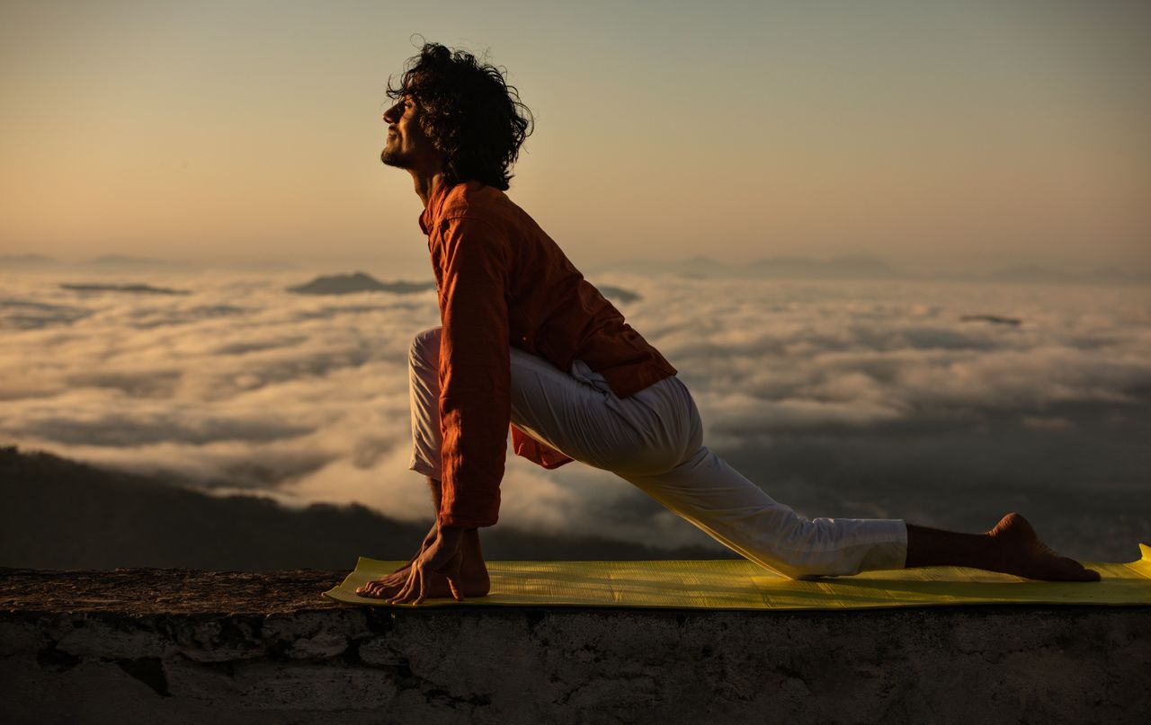 journey A man performing a yoga pose on a mat with a stunning sunrise backdrop over the clouds.