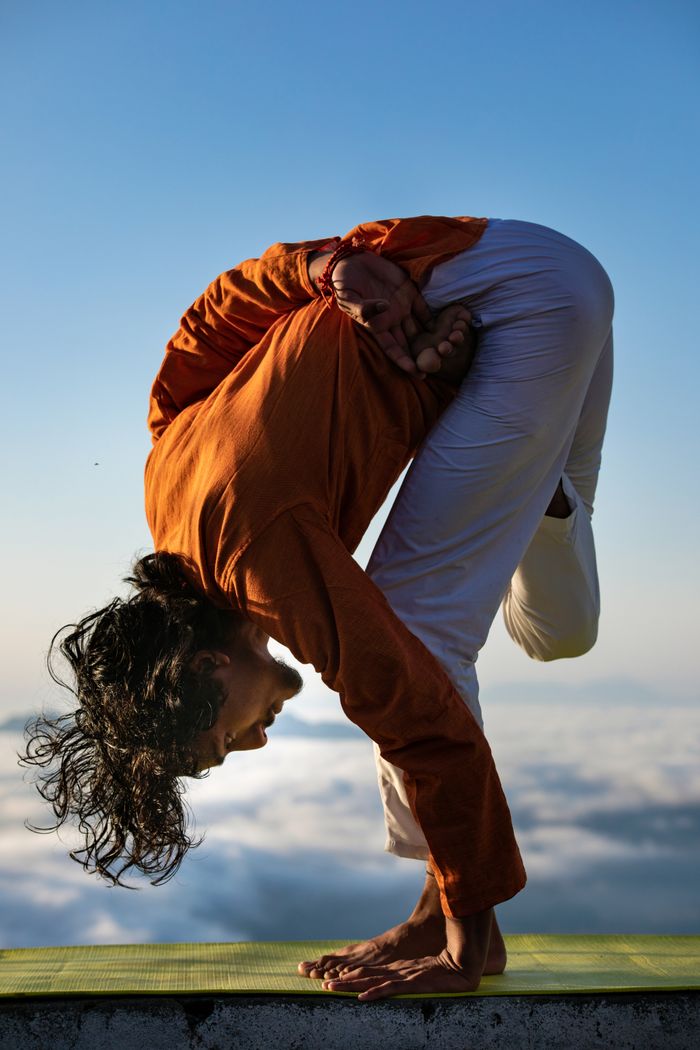 services-02 Man performing a challenging yoga pose outdoors against a blue sky and clouds.