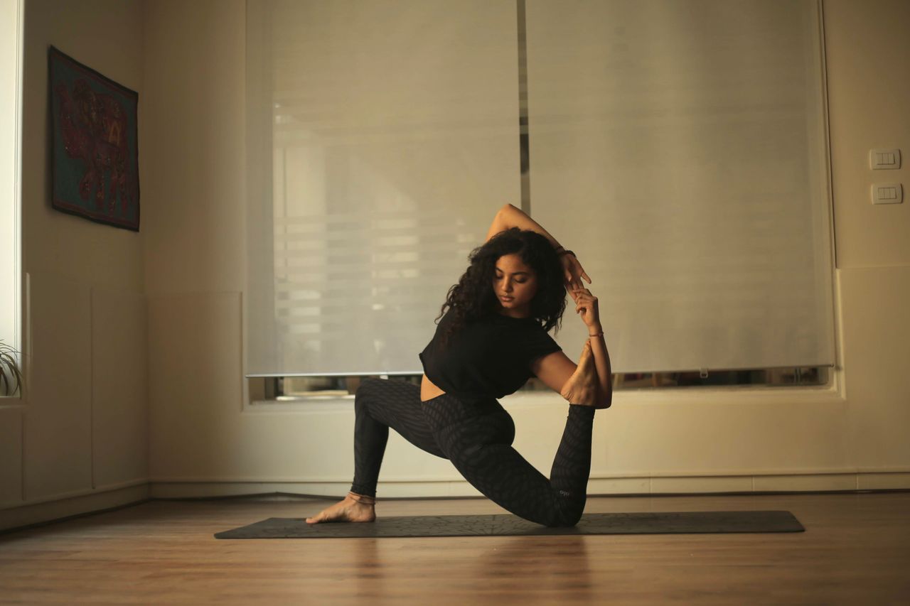 team-04 A woman in black attire performing a yoga pose on a mat indoors, showcasing flexibility and balance.