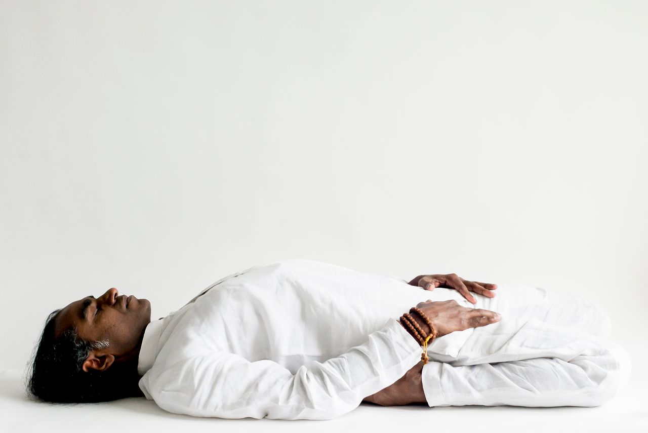 who-we-are A person in a white outfit practicing meditation, lying down peacefully indoors.